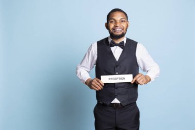 Otel görevlileri resepsiyonda resepsiyon göstergesi gösteriyorlar. Stüdyodaki beş yıldızlı tatil beldesinde misafirleri karşılıyorlar. Yetenekli profesyonel bellboy mavi arka plana işaret koyuyor..