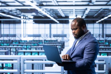 Veri merkezinde, yönlendiriciler, anahtarlar ve güvenlik duvarları gibi ağ altyapısını yapılandırmak için dizüstü bilgisayar kullanan işçiler. Sunucu odasında çalışan veri araştırmacısı, teknik arızalar arıyor