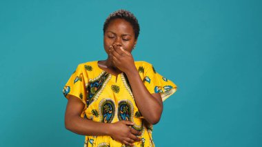 Kadın kendini çok yorgun hissediyor ve mavi arka planda esniyor. Stüdyoda uykusuzlukla uğraşan çok çalışan genç bir yetişkin. Yorgun ve bitkin bir yetişkin ve tükenmiş. Kamera A.