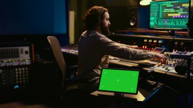 Ses tasarımcısı, ses seviyesini ayarlamak için karıştırma konsolu ve kaydırma çubukları kullanarak kontrol odasında kayıt ve işleme parçaları kullanıyor. Profesyonel stüdyoda yeşil ekran tabletle çalışan bir teknisyen. Kamera B.