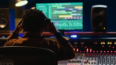 Sound designer editing tracks by adjusting volume levels with panel board knobs and sliders, studio control room. Audio technician mixing and mastering hit song with digital software. Camera A. clipart