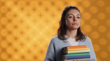 Portrait of upbeat woman holding pile of books, enjoying reading hobby for entertainment purposes. Radiant bookworm with stack of novels in arms enjoying leisure time, studio background, camera A clipart