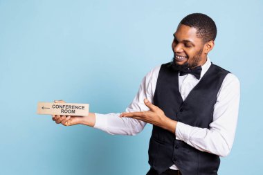 Hotel concierge staff holding the wall indicator for the conference room, providing directions for clients at five star resort. Bellhop doorman holds the pointer sign to the amenities. clipart