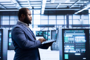 Veri merkezinde bilgisayar kullanan programcı gelişmiş teknolojiye sahip siber güvenlik ve etkin ağ yönetimini sağlıyor. Not defteriyle veri merkezi altyapısını optimize eden sunucu merkezinde profesyonel