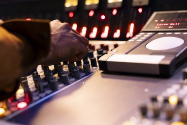 Afrikalı Amerikalı ses tasarımcısı kontrol odasında karıştırma konsolunu çalıştırıyor, ses ayarlarını ayarlamak için sürgülere ve düğmelere basıyor. Müzik mühendisi stüdyoda yeni şarkılar üretiyor. Kapat..