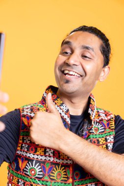 Happy man using cellphone to take selfies, doing thumbs up gesture. Jolly social media user taking photos using phone selfie camera, doing like hand gesturing, studio background clipart