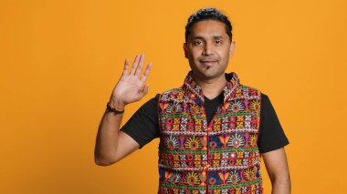 Portrait of jolly indian man with colorful garment smiling, looking pleased, isolated over studio background. Joyous person in traditional attire feeling carefree, camera A clipart