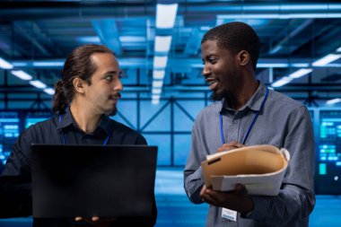 Smiling manager inspecting server room equipment, reading paperwork from folder, talking with employee. Supervisor doing evaluation of data center location, checking files clipart