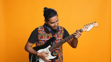 Elektro gitar tutan mutlu bir adam, rock müzik çalıyor, stüdyo arka planında izole edilmiş. Neşeli Hintli müzisyen müzik aleti kullanıyor, konser veriyor, şarkı söylüyor, kamera B