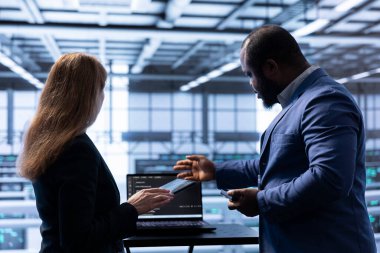 Yönetici ve yönetici, veri merkezinde afet kurtarma ve güvenlik protokolü planlaması yapıyor. İş arkadaşları, iş sürekliliğini sağlamak için sunucu odasında beyin fırtınası yapıyor.