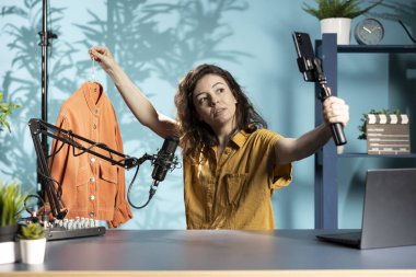 Moda içeriğini çeken bir kadın akıllı telefondaki selfie kamerasıyla hayran ceketini gösteriyor. Fashionista izleyicilere yeni giysiler sunuyor, malzemelerden bahsediyor, cep telefonuyla kayıt yapıyor.