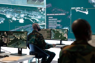 Askeri personel, izleme odasındaki büyük ekrandaki CCTV uydu görüntülerini inceliyor. Yeni bir savunma operasyonu üzerinde çalışıyorlar. Komuta merkezinde görev güvenliğini ve başarıyı sağlayan asker..
