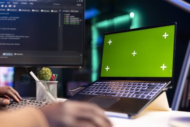 Afro-Amerikalı programcı yeşil ekranın yanında bulut hesaplama üzerinde çalışıyor, terminal penceresinde optimizasyon için kod yazıyor. IT mühendisi html kodu, sunucu güvenliği takmaya çalışıyor.