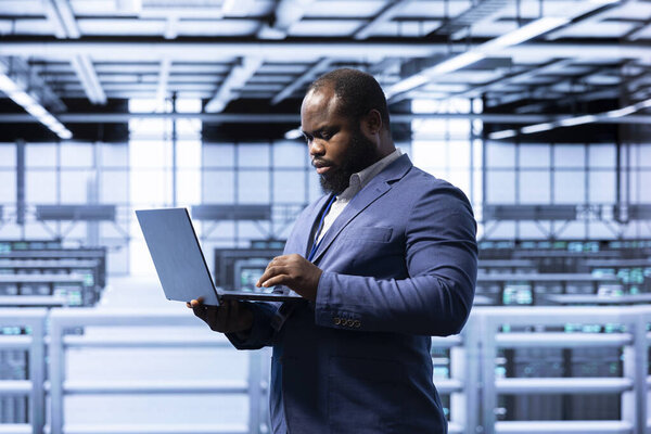 IT staff member in server hub using laptop to monitor energy consumption across supercomputer rigs. Computer scientist in data center making sure rackmounts are functioning optimally