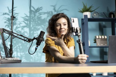 Neşeli kadın selfie çubuğunda akıllı telefon kullanarak profesyonel mikrofon sunuyor. Teknoloji içeriği yaratıcısı, stüdyo mikrofonunu hayranlarına gösteriyor, cep telefonuyla çekiyor