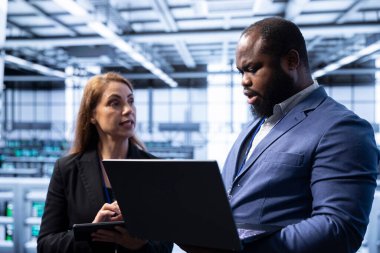 Sunucu merkezindeki çalışan, yönetici kurtarma planını dizüstü bilgisayarda gösteriyor, enerji tüketimini izliyor. Veri merkezinde beyin fırtınası yapan iş arkadaşları platformların en uygun şekilde çalıştığından emin oluyorlar.