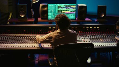 Müzik yapımcısı, kontrol odasında ses yazılımı ve karıştırma konsolu ile bir parça bitiriyor, sesleri işlemek için profesyonel stüdyoda teknik ekipmanlarla çalışıyor. Ses teknisyeni iş başında. Kamera B.