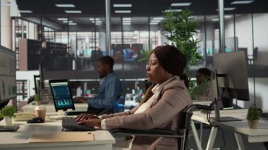 Finansal strateji üzerinde çalışan, organizasyonel amaçlara ulaşmak için veri analizlerini gözden geçiren Afrikalı Amerikalı bir çalışan. Kadın analist maluliyet dostu bir ofiste çalışıyor. Kamera B.