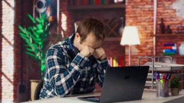 Oturma odasındaki yorgun adam dizüstü bilgisayardaki birçok e-postaya cevap vermek zorunda kalınca sinirlendi. Cihaz klavyesinde, kamera B 'de yazarken kendini yorgun hisseden serbest çalışan