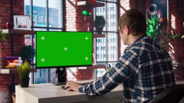 Oturma odasındaki tele-çalışan adam iş geliştirme planlamak için kroma anahtar bilgisayarı kullanıyor. Uzaktan çalışan proje araştırması yapıyor, yeşil ekran cihaz klavyesinde daktilo ediyor, kamera A