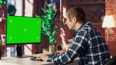 İş ortaklarının e-postalarını cevaplamak için kroma anahtar bilgisayarını kullanarak oturma odasındaki tele-işçi. İzole ekran aygıtı klavyesinde yazan uzaktan çalışan, apartmandaki görevleri çözen, kamera B