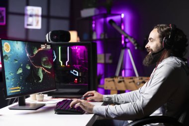 RGB 'nin aydınlattığı oturma odasından canlı yayında izleyicilerle sohbet eden gülümseyen adam. Kulaklık mikrofonuyla abonelerle konuşurken neşeli profesyonel oyuncu yayını oyunu