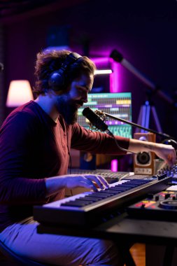 Yeni bir şarkı bestelemek, mikrofonda şarkı söylemek ve ses seviyelerini ayarlamak için piyano elektronik klavye çalan ses mühendisi. Yapımcı müzik kaydediyor, Midi kumanda takımında çalıyor..