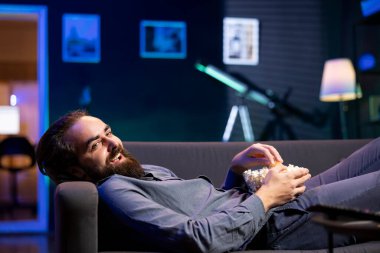 Kanepede uzanmış, aboneliğe dayalı komedi dizilerini abone olmak, patlamış mısırın tadını çıkarmak için TV 'yi kullanmış. Televizyondaki komik VOD şovlarına gülen, abur cubur yiyen bir adam.