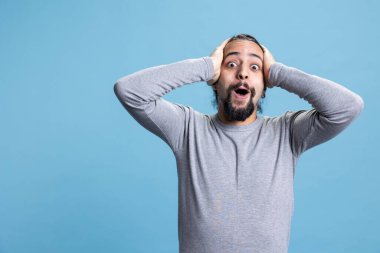 Şok olmuş, hevesli, genç bir yetişkin. Kamerada neşeli bir hava var. Mavi arka planda bir şeye şaşırmış ve heyecanlanmış. Gülümseyen mutlu insan coşkulu hissediyor.