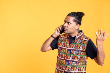 Disappointed indian man admonishing friend over debacle on call, negatively surprised by him, studio background. Upset person in disagreement with mate, rejecting arguments from his opponent clipart