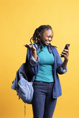 Radiant woman laughs, having funny conversation with friends during online teleconference using cellphone, studio background. Upbeat girl having fun with mates during internet videocall on phone clipart