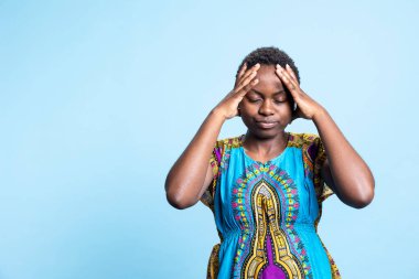 Afrika kökenli Amerikalı ciddi baş ağrısı çekiyor, mavi arka planda grip belirtileri gösteriyor. Genç bayan modelin sağlık sorunu ve ağrılı migreni var..