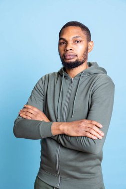 Portrait of confident smiling african american casual man posing with arms crossed, standing against blue background. Happy expressive person being friendly and optimistic in studio. clipart