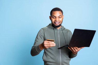 İndirimli kıyafet almak için internetten elektronik ödeme yapan kendine güvenen genç, alışverişkolik insan alışveriş çılgınlığından mutlu ve memnun. Neşeli neşeli adam internette ödeme yapıyor..