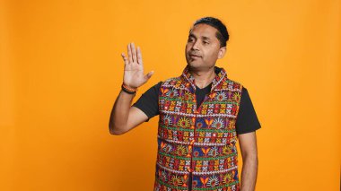 Indian man trying to stop chaotic fight using calming hand gesture to diffuse tensions, doing peaceful resolution. Reassuring person doing calm down sign gesturing, studio background, camera B clipart