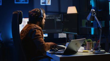 Daire ofisinde yazılım uygulaması geliştirmek için javascript programlama dili kullanan mühendis daktilo kodu. Görevleri bitirmek için çoklu monitör masaüstü kurulumu ve not defteri kullanarak yönetiyor, Kamera A