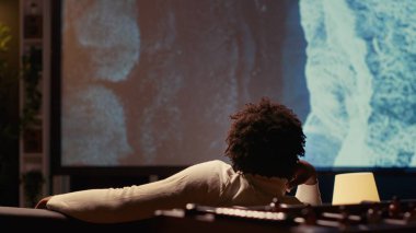 Modern video projektöründe çok güzel görüntü alan bir adam seyahat belgeseli izliyor. Ev sinemasında deniz manzarasının tadını çıkaran kişi, kanepede dinleniyor.