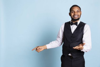 Doorman staff pointing at something to left or right sides in studio, indicating the direction for some amenities at the five star hotel. Bellboy porter wearing a suit and tie uniform on duty. clipart