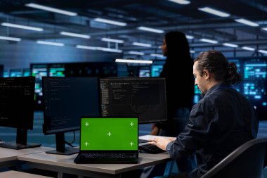 Veri merkezindeki yönetici, sunucuları yazılım zayıflıklarından korumak için sistemleri güncellemek için yeşil ekran dizüstü bilgisayar kullanır. IT uzmanı sunucuları etkileyen hataları bulmak için maket defteri kullanır
