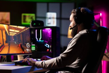 Bilgisayar masasındaki bilgisayarda, kulaklık kullanarak fütüristik bilim kurgu video oyunu oynayarak rahatlayan bir adam. Oyuncu, çevrimiçi çoklu oyunculu atıcıda lazerlerle düşmanları vuruyor.