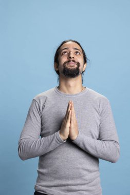 Erkek kişi elleri dua ederken poz veriyor ve kamerada Tanrı 'ya tapıyor, İsa Mesih' le konuşuyor ve Hıristiyanlığa inanıyor. Genç yetişkin, stüdyoda umutlu ve meditasyon yapıyor..