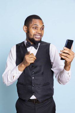 Gülümseyen kibar kapıcı stüdyoda online video çağrısına el sallıyor, konuklarla mavi arka plan hakkında bilgi paylaşıyor. Belboy personeli video konferans bağlantısında kravat ile.