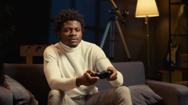 Odaklanmış BIPOC adamı, kontrol paneline spam saldırı tuşları atarak yoğun çevrimiçi video oyunu oynuyor. Oyuncu internet ihracat yarışmasına katılıyor, koltukta oturuyor ve oyun konsolunda oynuyor