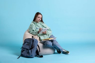 Saygılı genç kız armut koltuk üzerinde oturuyor, bilgi edinmek için okul notlarını gözden geçiriyor, stüdyo geçmişi var. Kollarında not defteri olan, kolej dersleri okuyan, sınavlar için araştırma yapan bir öğrenci.