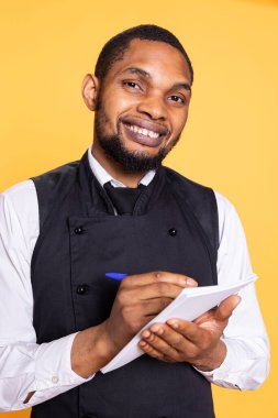 Dost canlısı restoran garsonu müşteriler için yemek siparişlerini not alıyor, fatura için not defterindeki bilgileri kullanıyor. Uşak müşteri memnuniyeti için insanlara hizmet ediyor..