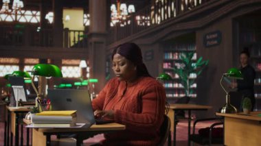 Afrika kökenli Amerikalı özel öğretmen okul kütüphanesinde ders için belge hazırlıyor ve öğrenme materyalleri hazırlıyor. Akademik kaynaklar sağlayan zeki profesör eğitim alanında akıl hocalığı yapıyor. Kamera A.