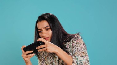 Akıllı telefondaki video oyunlarıyla eğlenen mutlu Hintli kadın, boş zamanların tadını çıkarıyor. Oyuncu telefonda oyundan zevk alıyor, düşmanları yenerken eğleniyor, stüdyo arka planında izole edilmiş, kamera B