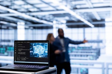 Yapay zeka veri merkezindeki yönetici ekibinin önünde dizüstü bilgisayardaki yapay zeka yazılımına odaklan. Yapay zeka sistemini güncelleyen işçilerin kullandığı yüksek teknoloji sunucu merkezindeki çalışma alanını kapat