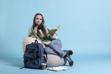 Ders kitaplarındaki kafa karıştırıcı bilgilerle kafası karışmış bir kızın portresi lise sınavlarına hazırlanıyor, stüdyo geçmişi var. Zor ev ödevleriyle kafası karışmış bir kadın, puf minder üzerinde jest yapmayı düşünüyor.