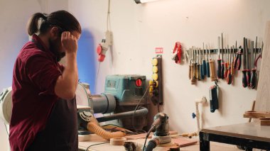 Esnaf, ahşaptaki kusurları temizlerken iş kazalarını önlemek için güvenlik gözlüğü kullanıyor. Yaralanmamak için koruyucu ekipman takan adam zımpara makinesiyle zımpara tahtası, kamera A 'yı kullanıyor.